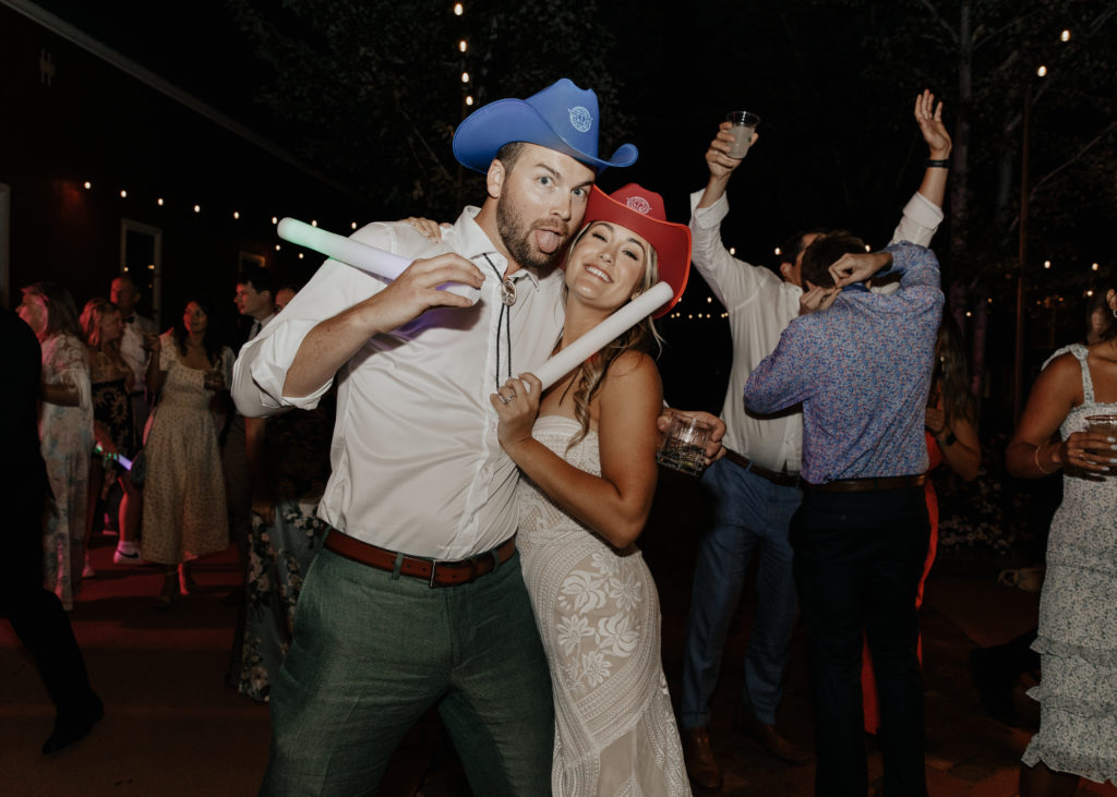 couple wearing cute cowboy hats with foam glow sticks for their wedding party props